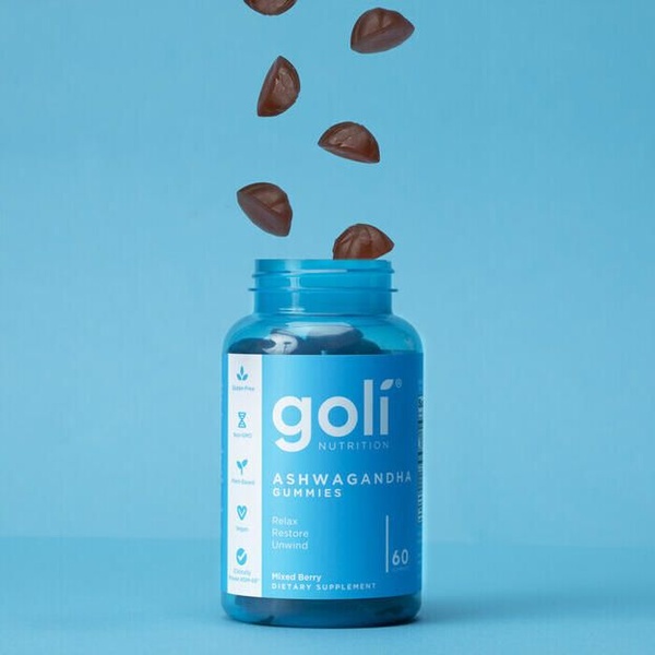 A high-clarity, minimalist product shot showing Ashwagandha gummies floating into a branded supplement bottle on a clean blue background.
